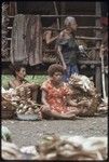 Mortuary ceremony: woman with baskets heaped with banana leaf bundles, bowl of uncooked taro