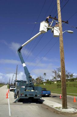 Using a truck with a gondola boom-arm lift, US Air Force (USAF) AIRMAN First Class (A1C) Sean Mackey, left, from Andersen Air Force Base (AFB), Guam and SENIOR AIRMAN (SRA) Thomas Manns, from Elmendorf AFB, Alaska, work to repair electrical lines