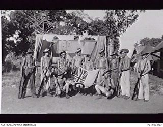 SAIDOR, NEW GUINEA. 1945-09-03. STAFF OF RAAF NORTHERN COMMAND HEADQUARTERS POSE WITH THE RAAF ENSIGN DURING CELEBRATIONS TO MARK THE SIGNING BY THE JAPANESE OF THE SURRENDER DOCUMENT AT MANILA THE ..