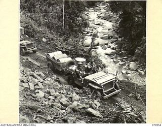 ZENAG, NEW GUINEA, 1944-02-27. A JEEP AND TRAILER CONVOY CONTINUING ALONG THE ROAD FOURTY EIGHT AND A HALF MILES FROM WAU AFTER THE SURFACE HAD BEEN CLEARED FROM A LANDSLIDE BY A D6 ANGLE DOZER ..