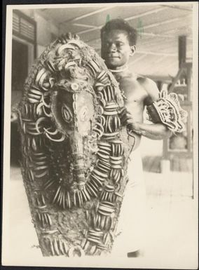 Man holding a large shield decorated with pig tusks, Awar, Sepik River, New Guinea, 1935 / Sarah Chinnery