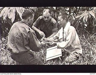 NADZAB, NEW GUINEA. 1943-09-20. UNITED STATES ARMY INTERPRETER SERGEANT MUNEKAWA (FOREGROUND) INTERROGATING A CHINESE COOLIE WHO HAD BEEN EMPLOYED BY THE JAPANESE, WHILE SX8960 CAPTAIN A. H. MCLAY ..