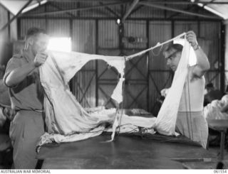 3 MILE, PORT MORESBY, NEW GUINEA. 1943-12-14. SX26055 LIEUTENANT L. G. GURNER, OFFICER COMMANDING (1) AND NX82290 CORPORAL K. J. WATSON (2); INSPECTING A LARGE RENT IN A SECTION OF A CARGO DROPPING ..