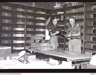 LAE, NEW GUINEA, 1945-12-21. MAJOR R. W. DELVES, DEPUTY ASSISTANT DIRECTOR OF AMENITIES FIRST ARMY, AND CORPORAL NETTE, LIBRARIAN, LOOKING THROUGH RECORD ALBUMS IN THE LIBRARY OF THE AUSTRALIAN ..