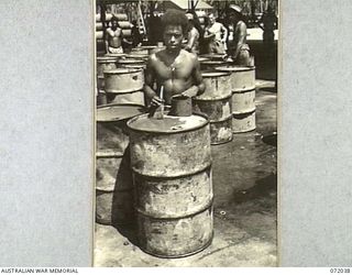 MILNE BAY, NEW GUINEA. 1944-04-04. A NATIVE BOY PAINTS OVER PREVIOUS BRAND AND BATCH NUMBERS ON 44 GALLON DRUMS AT THE 2ND AUSTRALIAN BULK PETROLEUM STORAGE COMPANY