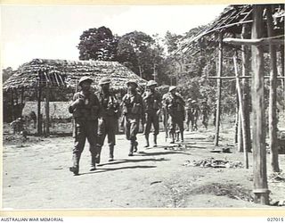 PAPUA, NEW GUINEA. 1942-10. MEN OF THE 2/33RD AUSTRALIAN INFANTRY BATTALION MARCHING THROUGH NAURO VILLAGE IN THE OWEN STANLEY RANGE, DURING THE ADVANCE OF THE 25TH AUSTRALIAN INFANTRY BRIGADE ..