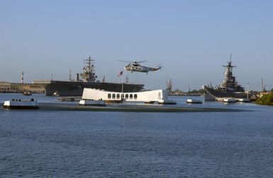 A US Navy (USN) SH-3H Sea King helicopter, Helicopter Combat Support Squadron 85 (HC-85, Golden Gaters), hovers over the Battleship USS Arizona (BB 39) Memorial (center, foreground) as the USN Nimitz Class Aircraft Carrier, USS RONALD REAGAN (CVN 76) arrives, with her crew manning the rails and rendering honors, on her maiden port visit to Pearl Harbor, Hawaii (HI), on the way to the Indian Ocean to participate in Operation UNIFIED ASSISTANCE, the humanitarian relief effort in response to the tsunami that devastated Southeast Asia on December 26, 2004. The battleship to the right is the USS Missouri (BB 63) Memorial