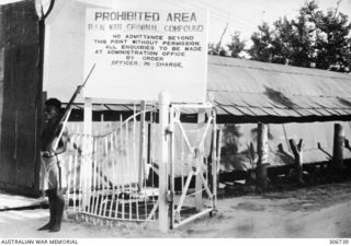 Manus Island. c.1948. A bare footed member of the Royal Papuan Constabulary on guard at the main entrance to the RAN War Criminal Compound. A sign at the front warns "Prohibited Area. RAN War ..
