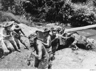 1943-03-10. NEW GUINEA. BRINGING UP SUPPLIES NEAR WAU. MANHANDLING A JEEP AND TRAILER THROUGH A BOGGY CREEK