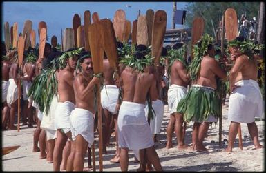 Groups of men in white lava lava holding wooden paddles