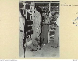 TOROKINA, BOUGAINVILLE. 1945-04-19. THE LIBRARY SUPERINTENDENT, MISS K. NOLAN (1), IN THE LIBRARY AT 2/1 GENERAL HOSPITAL. THIS LIBRARY IS ONE OF THE BEST TO BE FOUND AT ANY RED CROSS CENTRE