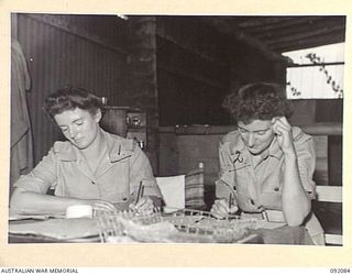 LAE, NEW GUINEA, 1945-05-21. CORPORAL D.M. O'CONNELL (1) AND SERGEANT T.A. HUSSEY (2), MEMBERS OF AUSTRALIAN WOMEN'S ARMY SERVICE CHECKING INVOICES IN THE AUSTRALIAN ARMY CANTEENS SERVICE, CANTEEN ..