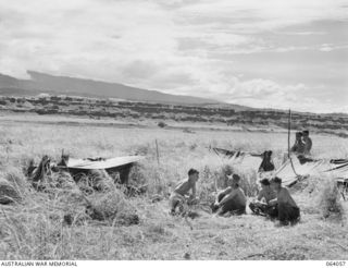 KELANOA AREA, NEW GUINEA. 1944-01-22. TROOPS OF THE 2/15TH INFANTRY BATTALION RESTING IN THE KUNEI GRASS NEAR THEIR ONE MAN SHELTERS (DOOVERS). THE TERRACED HILLS AND PART OF THE CROMWELL RANGES ..