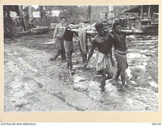 SOUTH BOUGAINVILLE. 1945-07-21. A BATTLE CASUALTY OF 15 INFANTRY BATTALION, PROTECTED FROM THE WEATHER BY A BANANA LEAF, BEING CONVEYED BY NATIVE STRETCHER BEARERS ALONG THE MUDDY BUIN ROAD TO THE ..