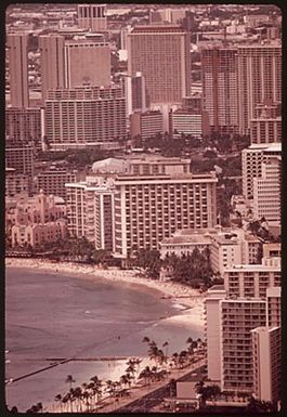 MASSED HIGHRISES OF WAIKIKI DISTRICT, FAVORITE OF TOURISTS SEEN FROM TOP OF DIAMOND HEAD, THE FAMOUS EXTINCT VOLCANO. THE WAIKIKI IMPROVEMENT ASSOCIATION HAS FORMED AN ARCHITECTURAL DESIGN REVIEW BOARD TO OVERSEE SUCH BUILDING, BUT IT IS PROBABLY TOO LATE. IN 1963 THERE WERE 9,203 HOTEL ROOMS IN ALL OF OAHU ISLAND. TODAY THERE ARE SOME 26,000 ROOMS, MOST OF THEM HERE IN WAIKIKI