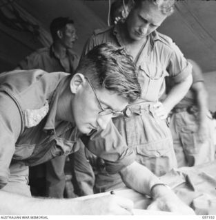 CAPE WOM, NEW GUINEA. 1945-09-27. PRIVATE E.G. MURPHY, 2/7 FIELD AMBULANCE (2), ATTENDING A SICK PARADE CONDUCTED BY CAPTAIN K. KEELY, MEDICAL OFFICER (1)