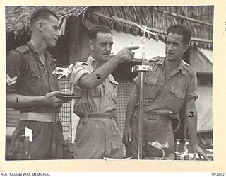 LAE AREA, NEW GUINEA. 1945-06-03. SAPPER P. COLLINS (2) EXPLAINING TO CORPORAL A. REID (1) AND CORPORAL J.A. FISHER (3), HIS CONSTRUCTION OF A PRIZE WINNING SMOKER'S STAND AT AN EXHIBITION OF ..
