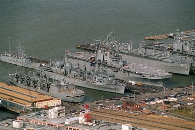 Aerial view of piers 4, 5 and 6 at the Norfolk Naval Base. The replenishment oiler USS Kalamazoo (AOR-6) is moored on the north side of pier 4. The fast combat support ship USS Supply (AOE-6) is moored at pier 5, south side of the Naval Reserve guided missile frigate USS Estocin (FFG-15) aft of her. The amphibious assault ship USS Saipan (LHA-2) is on the north side of the pier. The decommissioned destroyer tender Puget Sound (AD-38) is tied up on the south side of pier 6 awaiting removal to the James River Reserve Fleet. The amphibious assault ship USS Nassau (LHA-4) is moored on the north side with the guided missile frigate USS Robert G. Bradley (FFG-49)