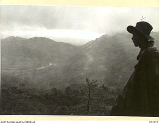 YAULA, NEW GUINEA. 1944-04-09. A MEMBER OF THE 57/60TH INFANTRY BATTALION VIEWING ALONG THE MINTJIM VALLEY TOWARDS BOGADJIM IN HEAVY RAIN SIX MILES AWAY