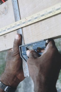 A member of Naval Mobile Construction Battalion 62 measures a board while helping to repair damage caused by Cyclone Uma