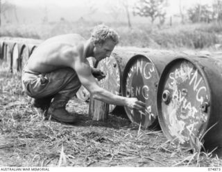 LAE-NADZAB, NEW GUINEA. 1944-07-20. PRIVATE W. PLUMMER, 2ND CORPS SALVAGE UNIT BRANDING DRUMS OF USED ENGINE OIL BEFORE SHIPMENT BACK TO THE MAINLAND FOR REFINING. DRUMS ARE MARKED AVIATION OR M.T. ..