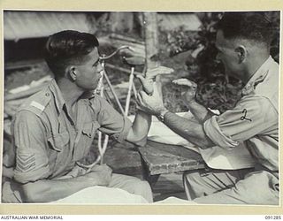 BOUGAINVILLE. 1945-04-26. SERGEANT W.J. KINNINMONT, 9 INFANTRY BATTALION (1), A PATIENT AT 2/3 CONVALESCENT DEPOT, DOING HAND EXERCISES UNDER THE DIRECTION OF LIEUTENANT T.G. RICE (2), TO RESTORE ..