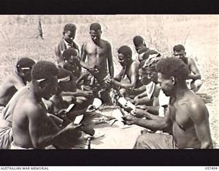 NADZAB, NEW GUINEA. 1943-09-20. NATIVE CARRIERS OF HEADQUARTERS, 21ST AUSTRALIAN INFANTRY BRIGADE PLAYING CARDS WHILE WAITING TO LOAD AIRCRAFT