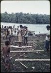 Canoe-building: men bring roughly shaped canoe to shore in Tukwaukwa village, pulling it across poles placed horizontally (bilabala)