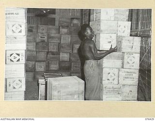 LAE, NEW GUINEA. 1944-10-04. LALAS, A NEW GUINEA NATIVE BOY WORKING IN THE SPIRIT STORE OF THE AUSTRALIAN ARMY CANTEENS SERVICE BULK STORE, NEW GUINEA DETACHMENT