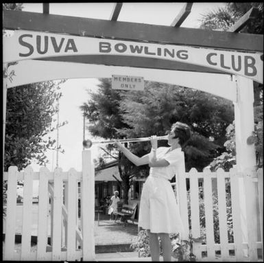 A woman drinking beer out of a yard glass in front of the entrance of the Suva Bowling Club, Suva, Fiji, November 1969 / Michael Terry