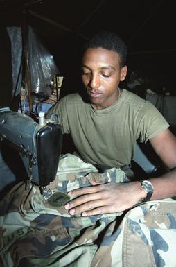 Private First Class (PFC) Richard Lee Taylor, 40th Supply and Service, sews a patch on a uniform during the 21st Infantry Division's annual Army training and evaluation program and field training exercise