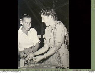 TOROKINA, BOUGAINVILLE ISLAND, SOLOMON ISLANDS. 1945-04-11. THE INTRICACIES OF MAKING STRING BELTS ARE BEING EXPLAINED BY RED CROSS ASSISTANT SUPERINTENDENT LYNNE DAVIES OF MELBOURNE, VIC, TO 77637 ..