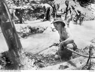 Finschhafen Area, New Guinea. 1943-10. Engineers digging out a creek to make foundations for a bridge on the main track from Finschhafen to forward areas. In the foreground Sapper C. S. Stevens of ..