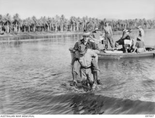 CAPTAIN W. DAVIES, MEMBER OF THE AUSTRALIAN SURRENDER PARTY FROM HEADQUARTERS 2 CORPS, BEING CARRIED ASHORE ON THE BACK OF A JAPANESE SOLDIER ON ARRIVAL AT NUMA NUMA PLANTATION. THE SURRENDER PARTY ..