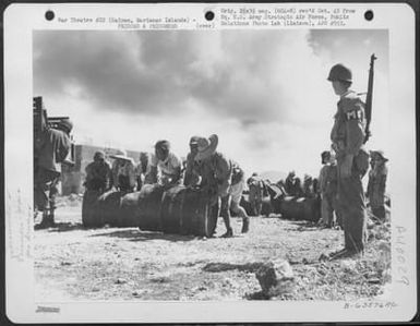 Japanese Soliders And Civilian Prisoners Of War Rolling And Stacking Gasoline Drums At A Supply Dump While Pvt. William E. Regan Of 170-01 91St Road, Woodhaven, Long Island, New York, Stands Guard. Saipan, Marianas Islands, 29 June 1944. (U.S. Air Force Number B63576AC)