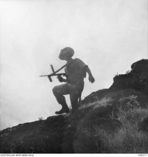 LALOKI VALLEY, NEW GUINEA, 1943-11-05. A SUB-MACHINE GUNNER, MEMBER OF THE PATROL OF THE NEW GUINEA FORCE TRAINING SCHOOL (JUNGLE WING) COMING OVER A CLIFF EDGE AT THE READY