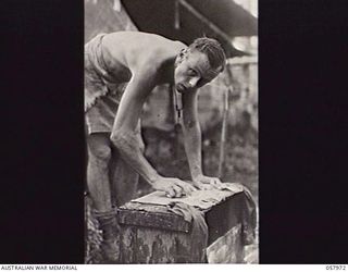 LAE, NEW GUINEA. 1943-10-04. VX38201 WARRANT OFFICER 1 R. B. IRVING, PHOTOGRAPHER, MILITARY HISTORY SECTION, WASHING HIS CLOTHES ON THE SCRUBBING BLOCK AT THE 5TH AUSTRALIAN DIVISION HEADQUARTERS