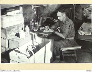 ALEXISHAFEN, NEW GUINEA. 1944-06-26. VX25080 WARRANT OFFICER II, D.H. SLINGO CHECKING THROUGH A LIST OF SUPPLIES IN THE Q STORE OF THE 2/15TH FIELD AMBULANCE