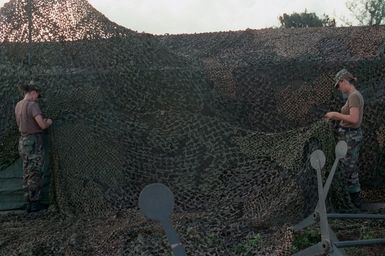 SPECIALIST (SPC) Lee and Private (PVT) Wyant, both assigned to the US Army (USA), 1ST Battalion, 17th Infantry Division set up camouflaged nets over tent facilities at Orote Point, Guam during Exercise TANDEM THRUST '99