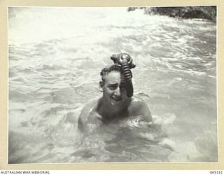 KILIGIA, NEW GUINEA. 1944-03-20. MR. PAUL BECKER OF THE AUSTRALIAN PUBLIC RELATIONS FIELD UNIT IN THE WATER, WITH HIS BREATHING APPARATUS SITTING ON HIS HEAD
