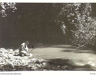 FINSCHHAFEN AREA, NEW GUINEA. 1944-04-09. QX44130 CAPTAIN J.L. GROOM (1), COMMANDING OFFICER 15TH MALARIA CONTROL UNIT, AT THE EDGE OF THE QUOJA RIVER. ALTHOUGH ONLY A FEW HUNDRED YARDS FROM THE ..