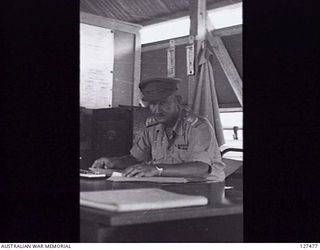 LAE, NEW GUINEA. 1945-12. SX30147 LIEUTENANT COLONEL J. W. K. BEDDOME, CHIEF ORDNANCE OFFICER, 4 ADVANCED ORDNANCE DEPOT, SITTING AT HIS DESK