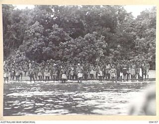 TINIAN, BOUGAINVILLE. 1945-07-18. NATIVES SINGING FAREWELL ON THE BEACH AS FLIGHT LIEUTENANT N.C. SANDFORD, ALLIED INTELLIGENCE BUREAU, LEAVES BY CANOE TO BOARD THE MOTOR LAUNCH ML1327, ON THE ..