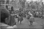 Mortuary ceremony, Omarakana: mourning women in long fiber skirts, faces and bodies covered with ash and heads shaved, hold banana leaf bundles