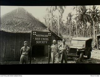 Milne Bay, New Guinea. 1943-06. Left to right: Unknown, Sol Cohen, Australian Red Cross Society (ARCS), unknown, standing beside an ARCS sign in front of the their hut. Note the ARCS jeep at right