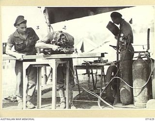 LAE, NEW GUINEA, 1944-03-24. MEMBERS OF THE 2/125TH BRIGADE WORKSHOP ATTACHED TO THE 7TH DIVISION PICTURED USING EQUIPMENT. QX14091 CORPORAL J. H. GAY (1), IN THE BACKGROUND, ELECTRICALLY ARC WELDS ..
