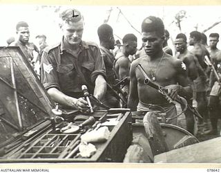 BOUGAINVILLE ISLAND. 1945-01-25. QX34754 SERGEANT R.J. TROTT, ARMOURER OF "A" COMPANY, 1ST NEW GUINEA INFANTRY BATTALION (1) TESTING THE OWEN GUN OF PN882 PRIVATE KORO (2) DURING A ROUTINE WEAPON ..
