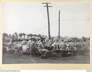 JACQUINOT BAY, NEW BRITAIN, 1945-08-23. THE ROYAL NEW ZEALAND AIR FORCE STATION BAND PLAYING BETWEEN RACES AT THE VICTORY CUP RACE MEETING HELD ON THE AIRSTRIP USING WOODEN HORSES CONTROLLED BY THE ..