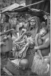 Mortuary ceremony, Omarakana: mourning woman holds large pile of banana leaf bundles at ritual exchange