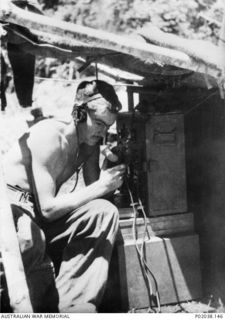 NX142537 Signalman James (Jim) Pashley, a member of a signals unit attached to the 16th Brigade, listens to a radio under a makeshift cover on the Kokoda Track. (Original housed in AWM Archive ..